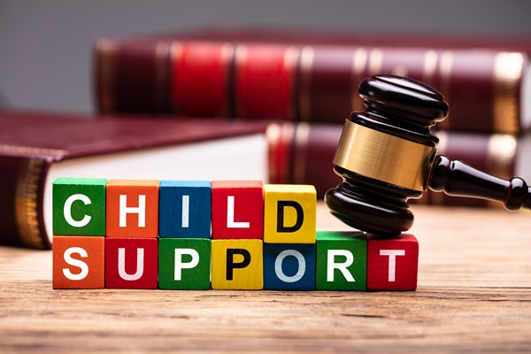Wooden blocks spelling "Child Support" with a judge’s gavel resting on top, placed on a wooden desk with legal books in the background. (269760363)