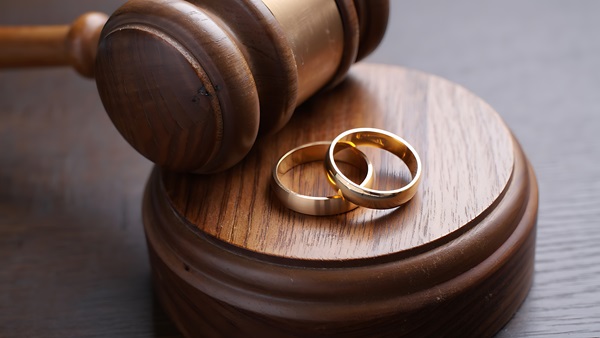Two gold wedding bands resting on a wooden judicial sound block next to a judge's gavel, symbolizing the legal dissolution or annulment of a marriage in New Jersey.